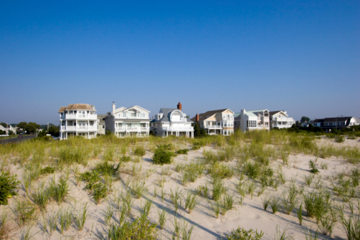 Color DSLR picture of luxury, white vacation beach houses along the Spring Lake, New Jersey shore, with sand dunes in the foreground and a clear, bright, daytime blue sky background.  Horizontal orientation with ample copy space for text.