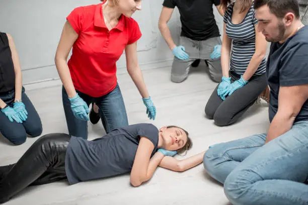 Young woman instructor showing how to lay down a woman during the first medical aid training indoors