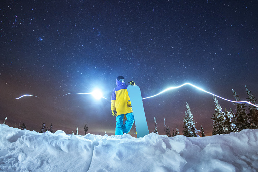 Lady snowboarder stands against abstract mountains and stars at night sky