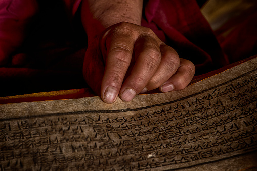 Hands of a Tibetan monk with an ancient prayer book while he is reading in the assembly hall of a monastery in Central Tibet.