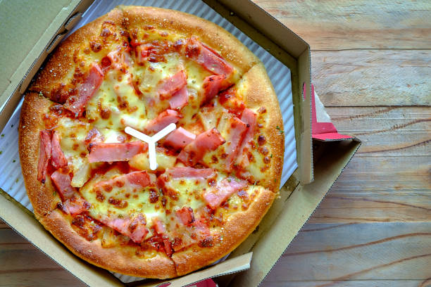 istock Delicious pizza with pineapple, ham slice, bacon slice, mozzarella cheese, pizza sauce in a delivery box on wooden background for fast food and ready to eat concept 929941050