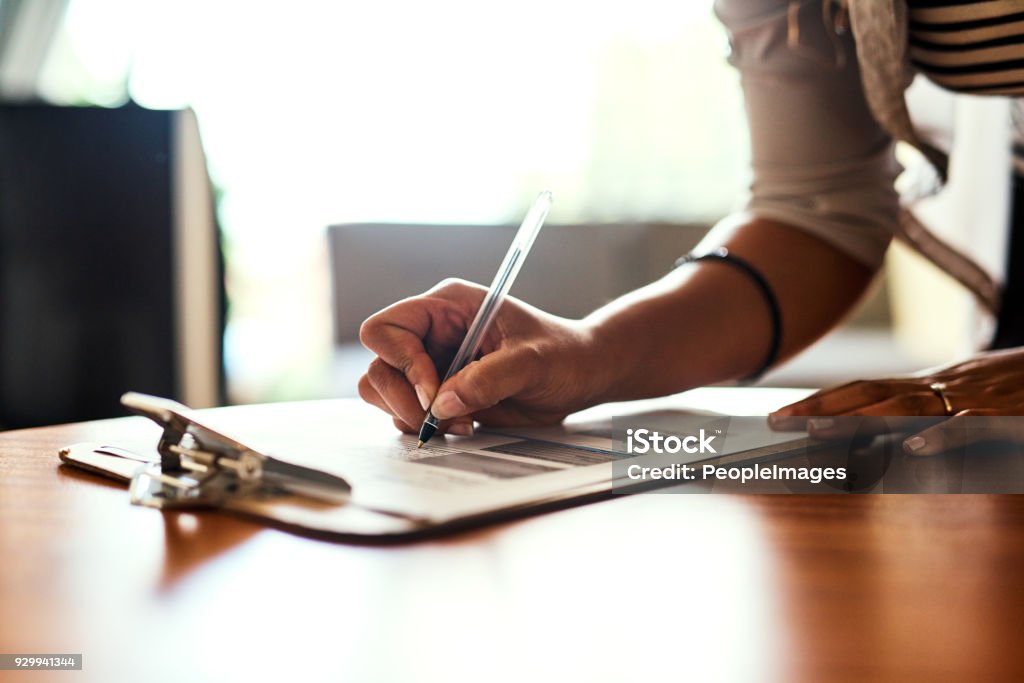 Filling out an important form Closeup shot of an unrecognizable woman filling in paperwork at a table Clipboard Stock Photo