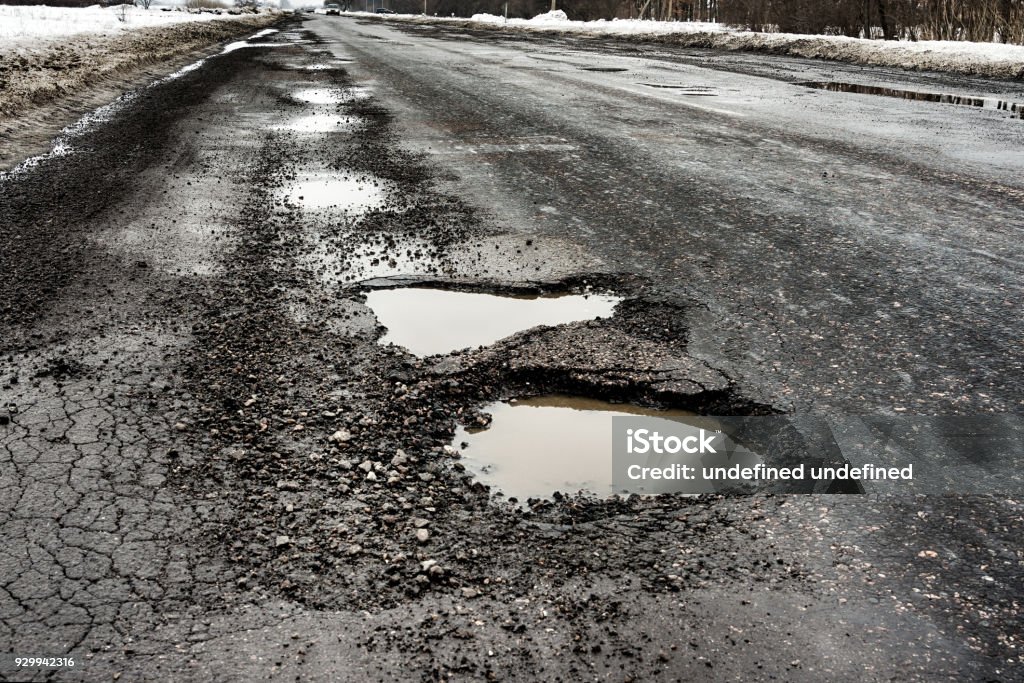 old highway with holes and snow. Landscape road potholes in cloudy winter weather. concept absence of timely repair of highway. old highway with holes and snow. Landscape road in the potholes in cloudy winter weather. The concept of the absence of timely repair of the highway. Pot Hole Stock Photo