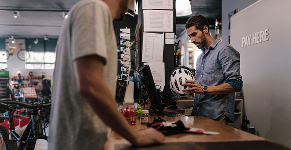 Man at the billing counter selling a bicycle helmet. Sport shop owner making a bill for sale of helmet using computer.