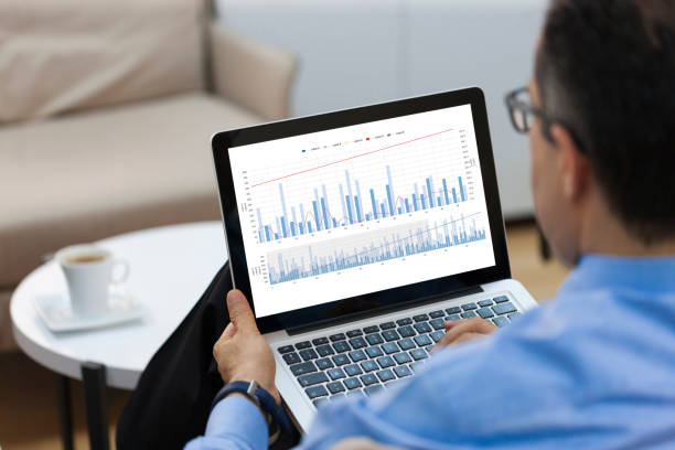 geschäftsmann sucht finanz-charts auf laptop - einzelner mann über 40 grafiken stock-fotos und bilder