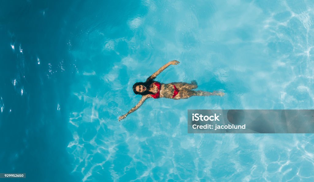 Woman enjoying swimming in a pool Aerial view of woman swimming in resort pool. Top view of female enjoying swimming in a pool. Swimming Pool Stock Photo