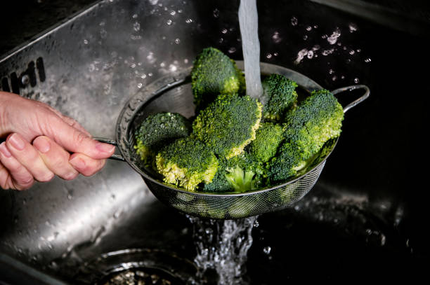 istock Woman's hand washing broccoli under running water at the kitchen sink. 929955822