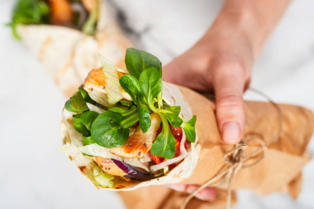 istock Woman's hand holding a fresh tortilla wrap tied round with brown paper and string. 929961124