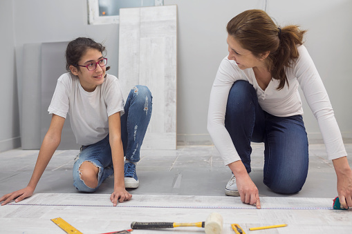Mature Woman Installing Laminate Floor With Her Cheerful  Teenage Daughter