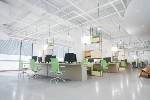 Interior of a large empty modern office with green chairs and wooden desks.