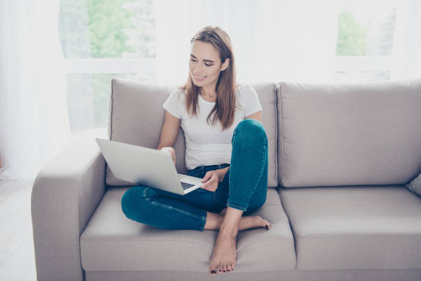 istock Serene gorgeous brown haired student on the beige couch at home studying, chilling, so comfortable, in fashioanble white outfit, denim pants, so nice light design interior indoors 929990270