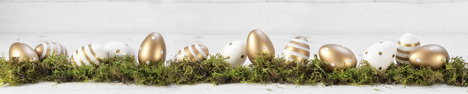 easter decoration, gold painted eggs on moss against a gray white wooden background, extra wide panoramic banner, copy space, selected focus