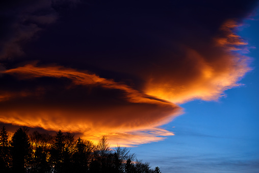 close up view of a huge storm passing above the land at night seen from afar from the countryside. orange city lights illuminating the clouds. lightnings striking inside the clouds and creating blue shades of colors