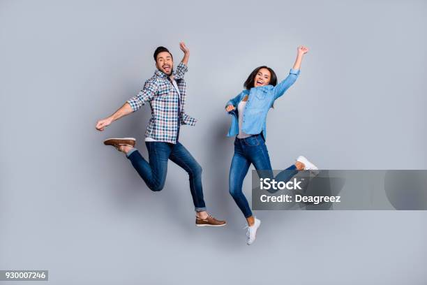 Photo libre de droit de Il A Vs Portrait Pleine Longueur She Du Couple Attractif Ludique Joyeux Comique En Tenue Décontractée Jeans Chemises Sautant Sur Fond Gris banque d'images et plus d'images libres de droit de Sauter