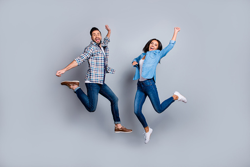 He vs She full length portrait of attractive, playful, cheerful, comic couple in casual outfit, jeans, shirts jumping  over grey background