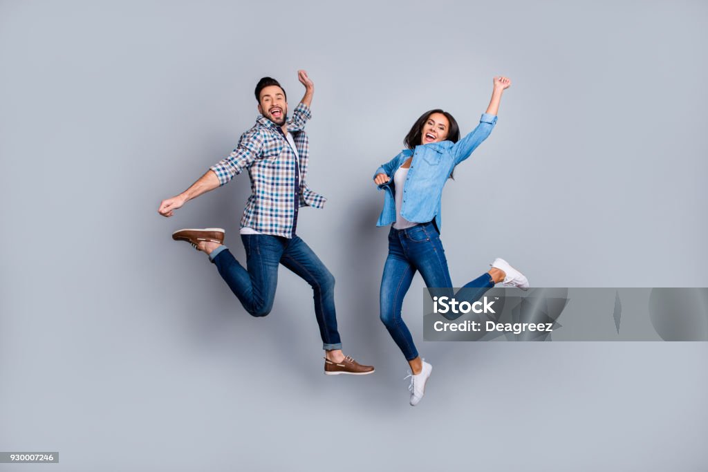 He vs She full length portrait of attractive, playful, cheerful, comic couple in casual outfit, jeans, shirts jumping  over grey background Jumping Stock Photo