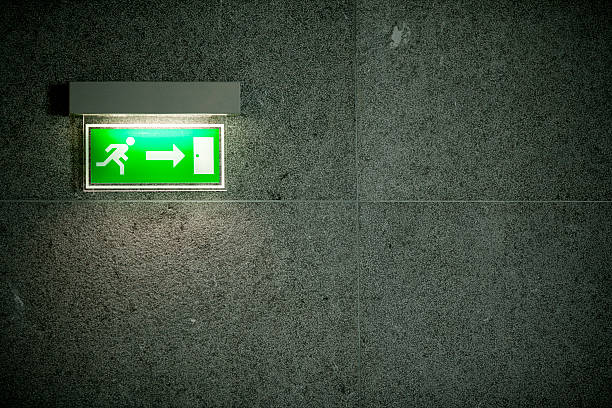 Illuminated green exit sign on dark large stone tile wall stock photo