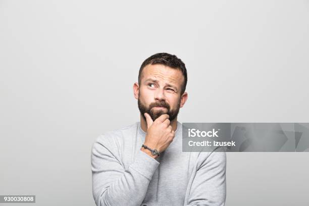 Portrait Of Worried Bearded Young Man Looking Up With Hand On Chin Stock Photo - Download Image Now