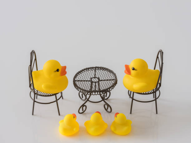 istock Two yellow rubber ducks facing and talking to each other whilst sitting at a table, with three smaller/young ducks listening below the table.. 930034484