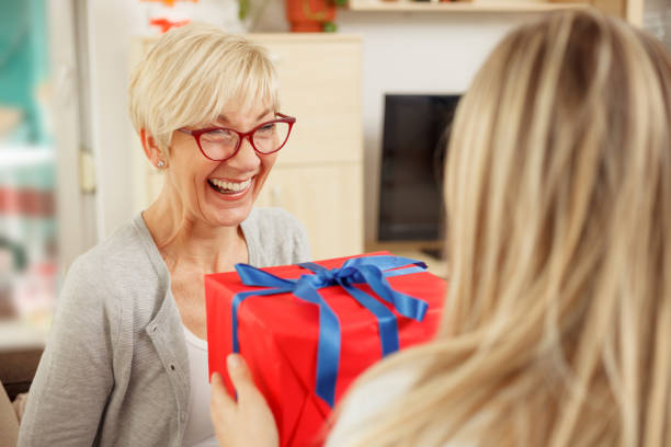 młoda kobieta zaskakuje swoją matkę pudełkiem prezentowym - gift mothers day birthday giving zdjęcia i obrazy z banku zdjęć