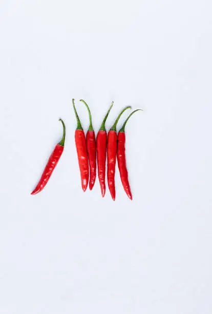 Food background of bunch of fresh hot spicy bird's eye chillis on white background, with one sticking out odd one out, plenty of copy space