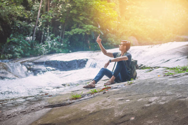 istock Hiker backpack travel and online working with his phone at  waterfall  the forest. 930072660