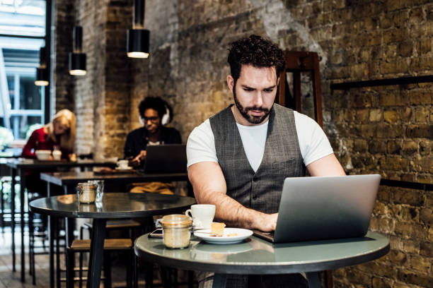 istock Mid adult man sitting at table in cafe and using laptop 930090034