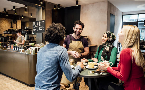 istock Cheerful waiter talking to thee customers in cafe and smiling 930090066
