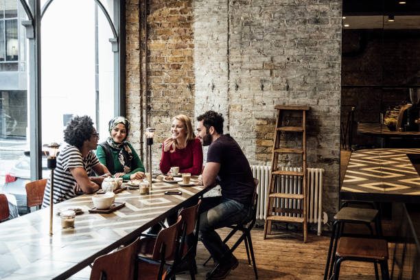 Four friends sitting at long table in cafe by window talking