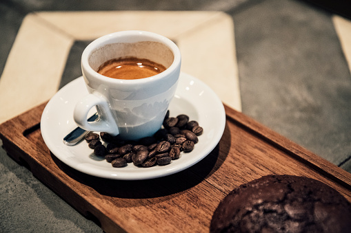 Cup and saucer on wooden board in cafe, small strong black coffee, roasted beans