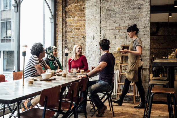 Waitress serving customers in cafe Four friends sitting at table waiting for young woman to bring food and drink english cuisine stock pictures, royalty-free photos & images