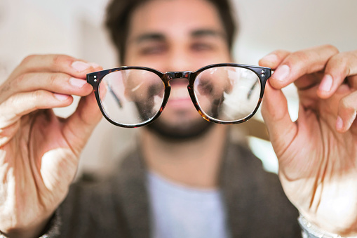 Man choosing glasses in optical store using mirror