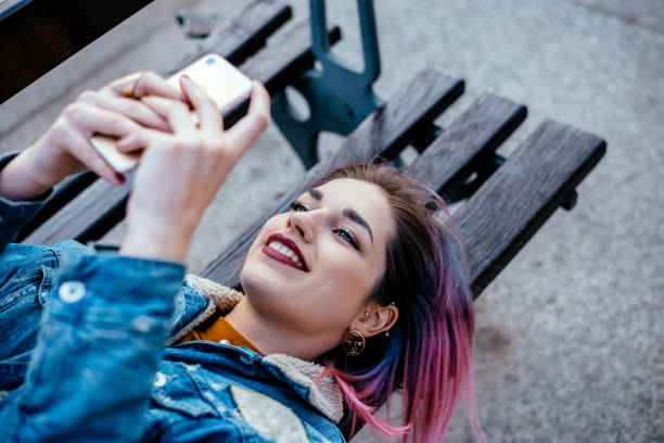 istock Girl with dyed hair using phone while lying on a bench. 930115754