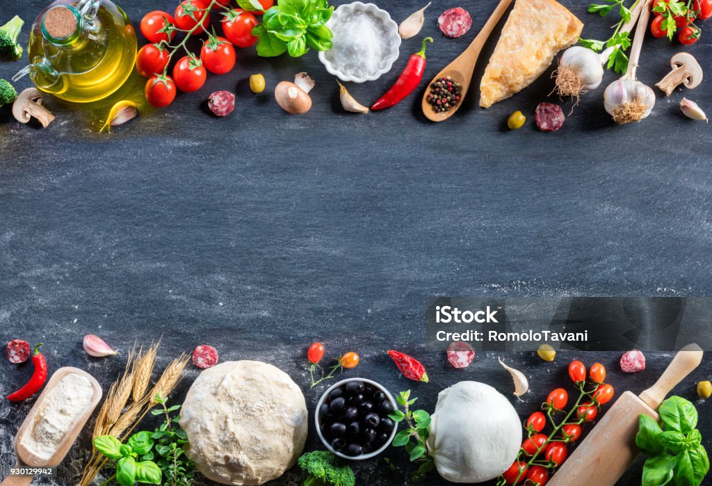 Pizza Ingredients On Black Table In A Raw - Italian Food Ingredients For Making Pizza on Stone Copper Mortar With dough Fresh Basil, Olive Oil, Garlic, Tomato, And Mozzarella Ingredient Stock Photo