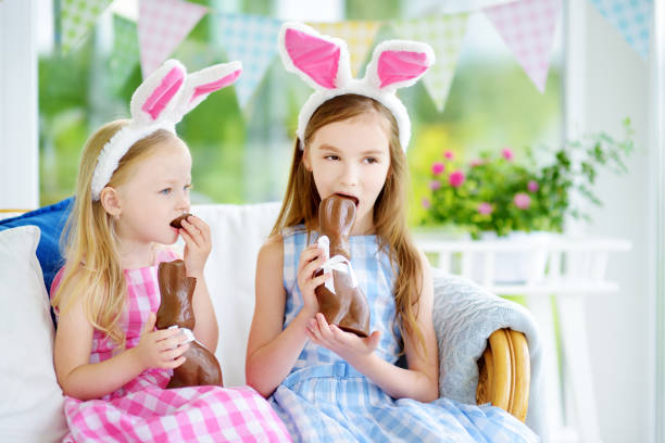 deux mignonnes petites sœurs portant des oreilles de lapin, manger des lapins de pâques au chocolat. enfants jouant oeuf chassent sur pâques. - figurine easter egg easter holiday photos et images de collection