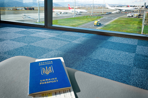 Tbilisi, Georgia, 2017-12-07: Ukrainian foreign passport with tickets is on chair at the airport with a view of plane and landscape. Concept traveling, right to travel, free movement and visa free.