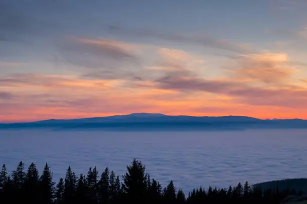 View from mountain Schoeckl in Styria over low stratus to mountain ranges Koralpe and Pack to sunset