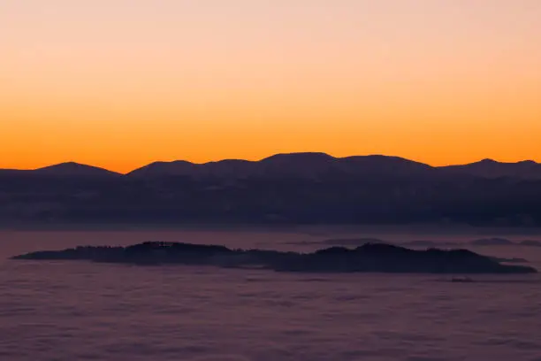 View from mountain Schoeckl over low stratus to mountain range Pack with Speikkogel and Ameringkogel to sunset