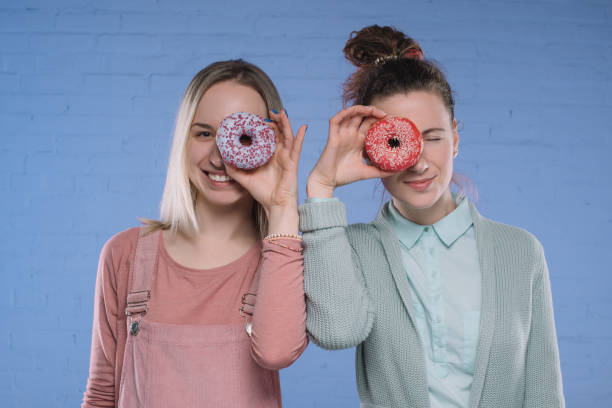 istock smiling young women covering eyes with glazed doughnuts 930264400