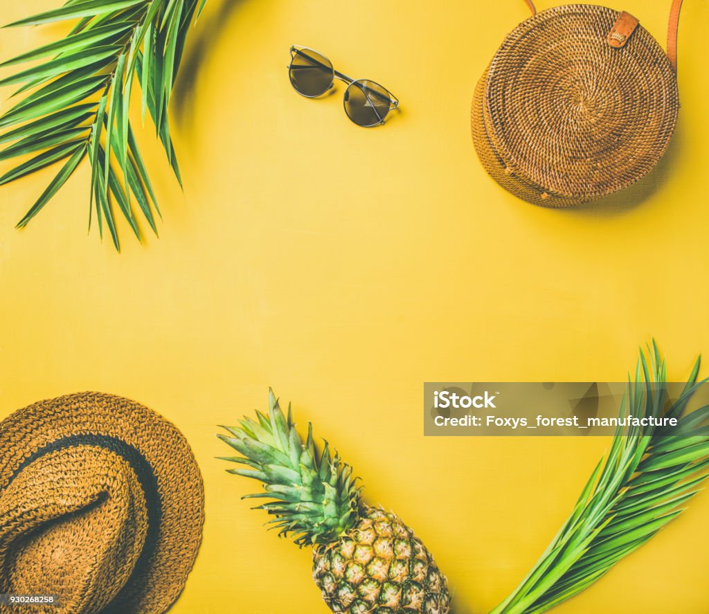 Colorful summer fashion outfit flat-lay Colorful summer female fashion outfit flat-lay. Straw sunhat, bamboo bag, sunglasses, palm branches and pineapple over yellow background, top view, copy space. Summer fashion or holiday travel concept Summer Stock Photo