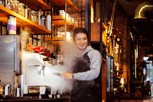 A young barista is preparing coffee for customers at his cafe counter.