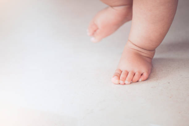 kleine babys füße tun den ersten schritt auf dem boden - baby toe stock-fotos und bilder