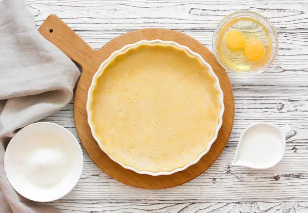 Dough for baking tart (quiche) and baking ingredients above flour, eggs and cream. Top view