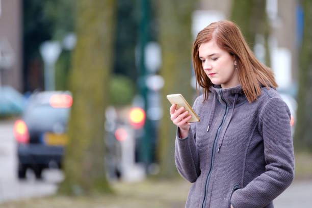 young woman looks at her cell phone young woman checked her cell phone for new messages outdoors Distracted stock pictures, royalty-free photos & images