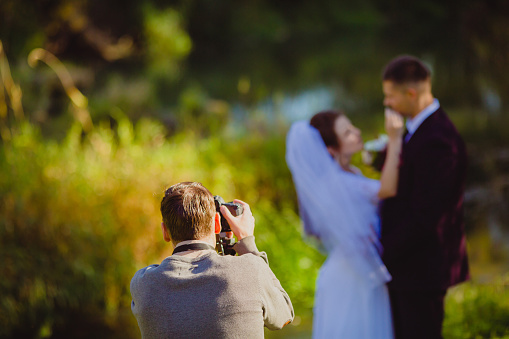 Photographer taking Pictures of the Bride and Groom in the summer park