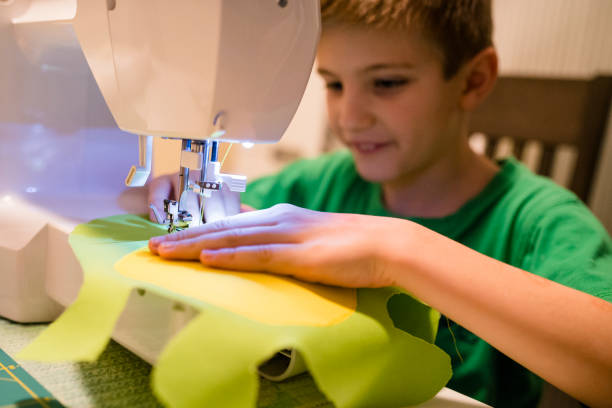 jeune garçon apprend à coudre sur une machine à coudre électrique - machine sewing white sewing item photos et images de collection