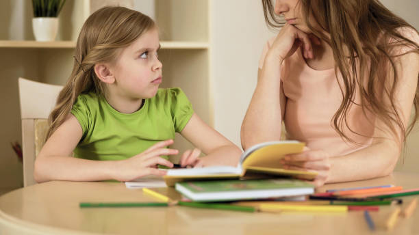 istock Upset little girl with misunderstanding looking at her mother doing school tasks 930436806