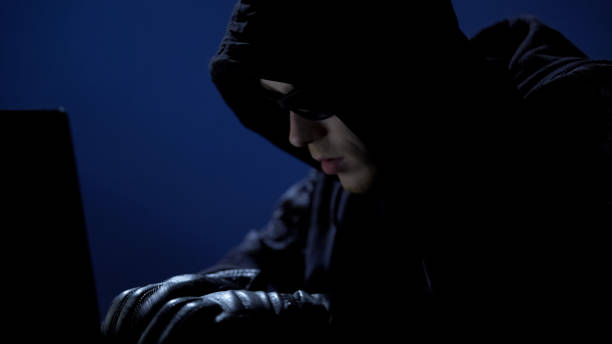 istock Strange man in black clothes, sunglasses and gloves stealing data from laptop 930441116