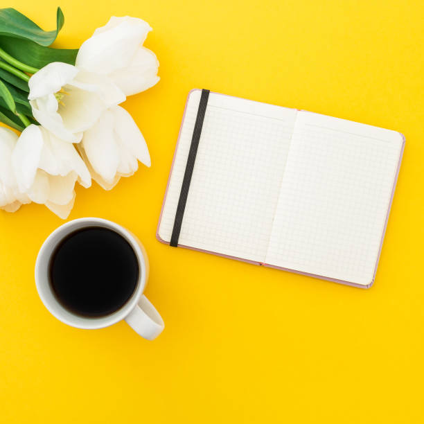 istock White tulips, notebook with mug of coffee on yellow background. Flat lay, top view. 930458782
