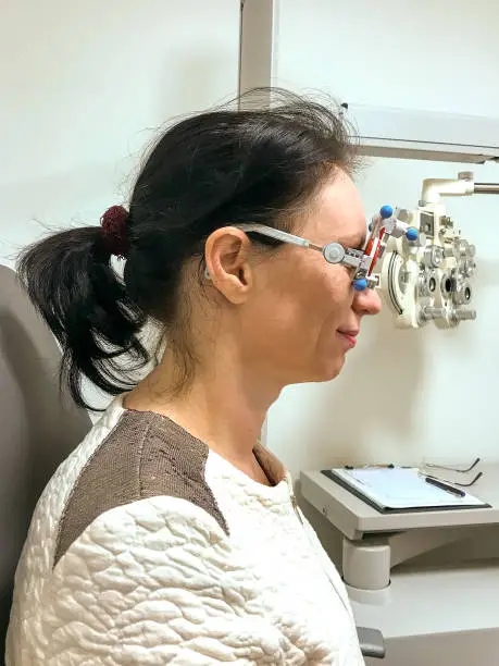 Woman being tested for new eyeglasses at an optometrist using equipment with interchangeable corrective lenses to measure her acuity